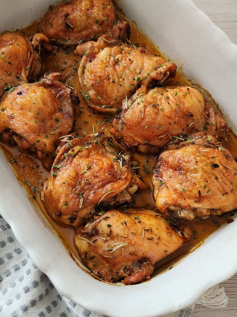 Juicy herb chicken thighs baked until golden brown in a white ceramic baking dish