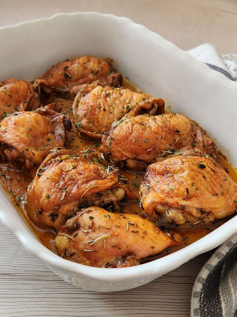 Juicy herb chicken thighs baked until golden brown in a white ceramic baking dish