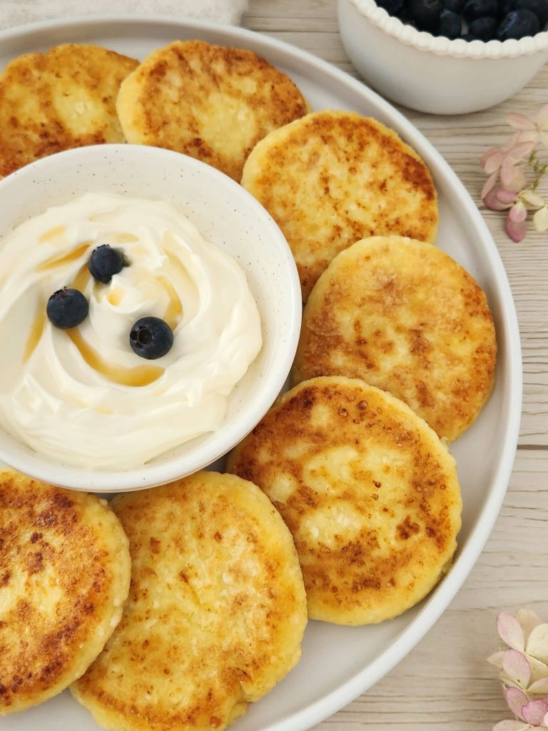 Golden cottage cheese pancakes served on a white plate with yougurt and blueberries
