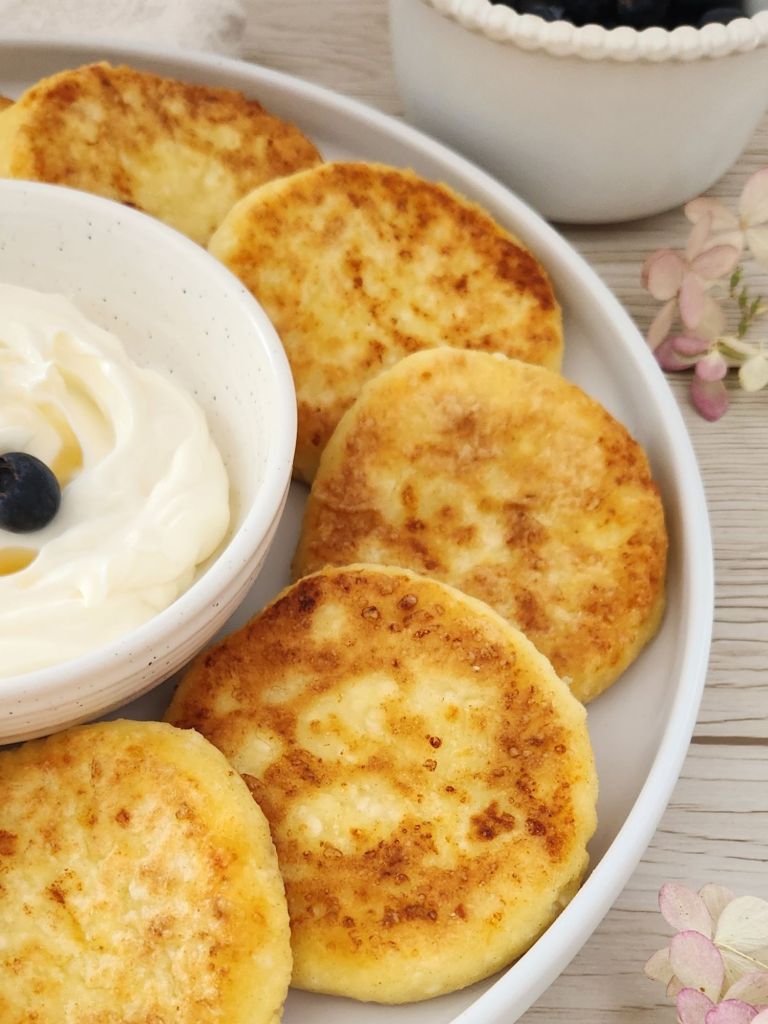 Golden cottage cheese pancakes served on a white plate with yougurt and blueberries