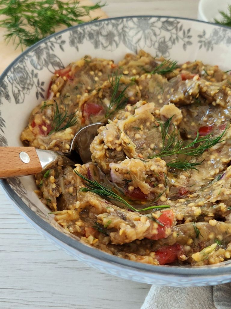 Creamy roasted eggplant dip with tomatoes, red onion, garlic, olive oil and fresh dill in a rustic bowl.