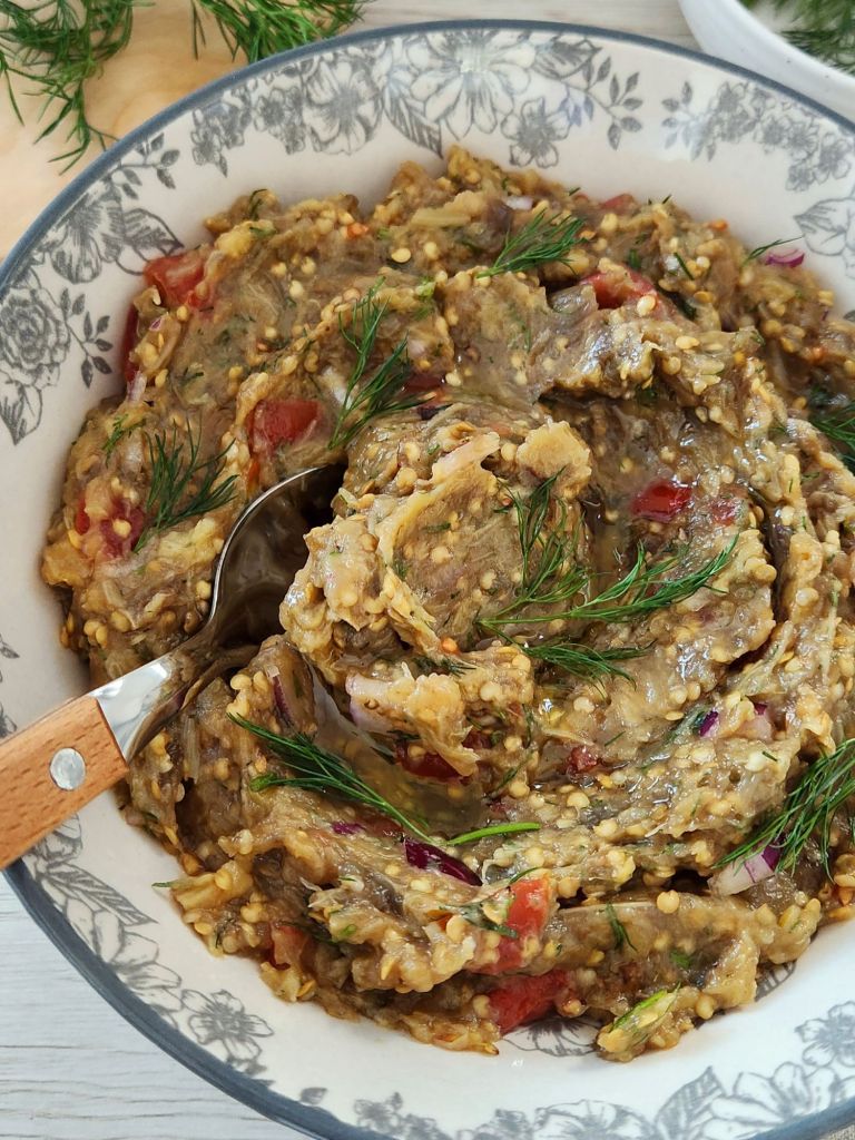 Creamy roasted eggplant dip with tomatoes, red onion, garlic, olive oil and fresh dill in a rustic bowl.