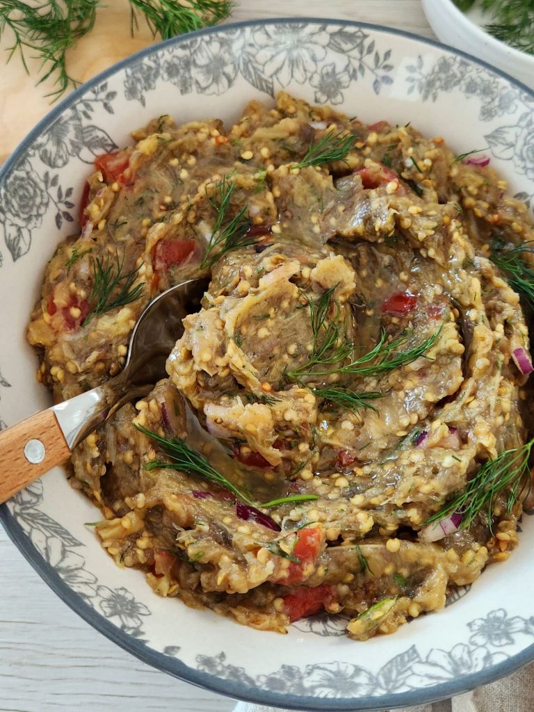 Creamy roasted eggplant dip with tomatoes, red onion, garlic, olive oil and fresh dill in a rustic bowl.