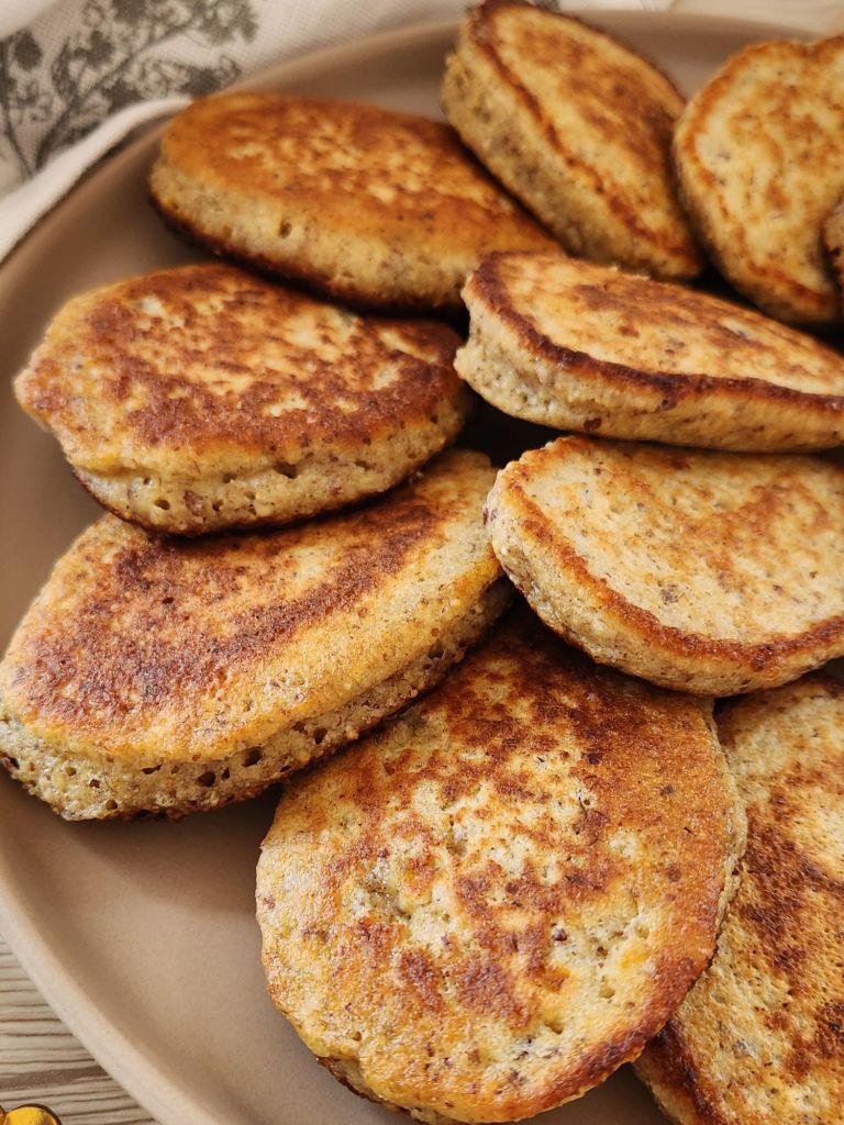 Fluffy golden pancakes made with oat flour, eggs, and banana, served warm with fresh banana slices on a plate.
