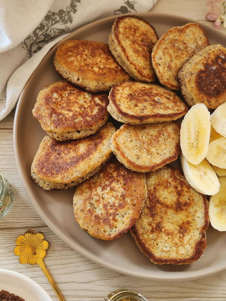 Fluffy golden pancakes made with oat flour, eggs, and banana, served warm with fresh banana slices on a plate.