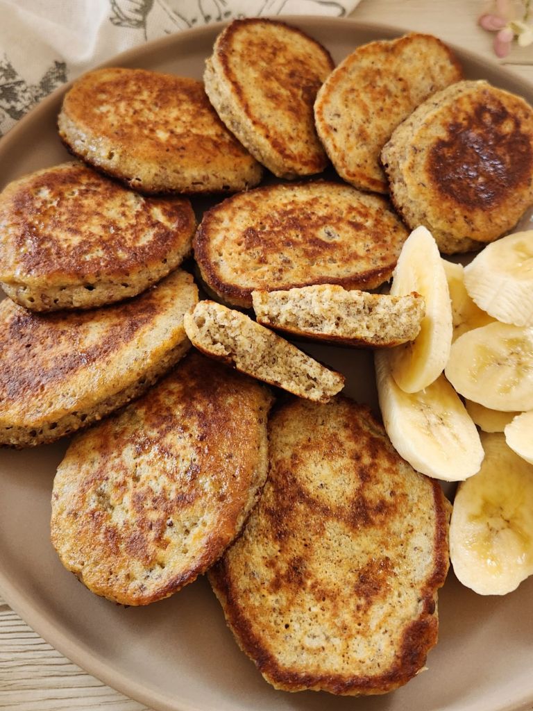 Fluffy golden pancakes made with oat flour, eggs, and banana, served warm with fresh banana slices on a plate.