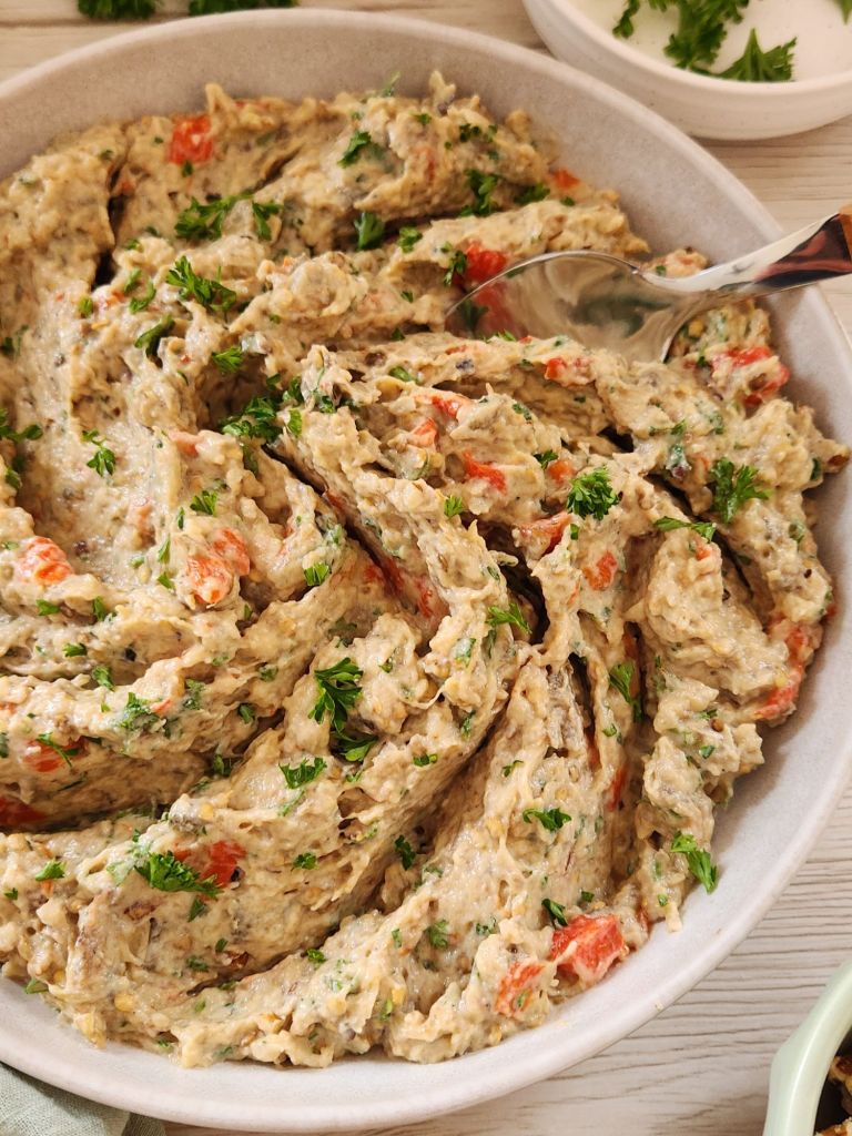 Creamy Eggplant Tahini Salad with roasted bell pepper, walnuts and parsley served in a beige bowl.