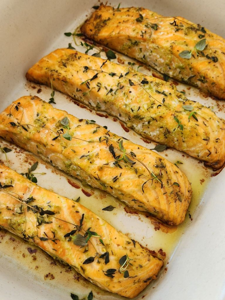 Fillets of baked salmon with basil, thyme and slices of lemon in baking dish