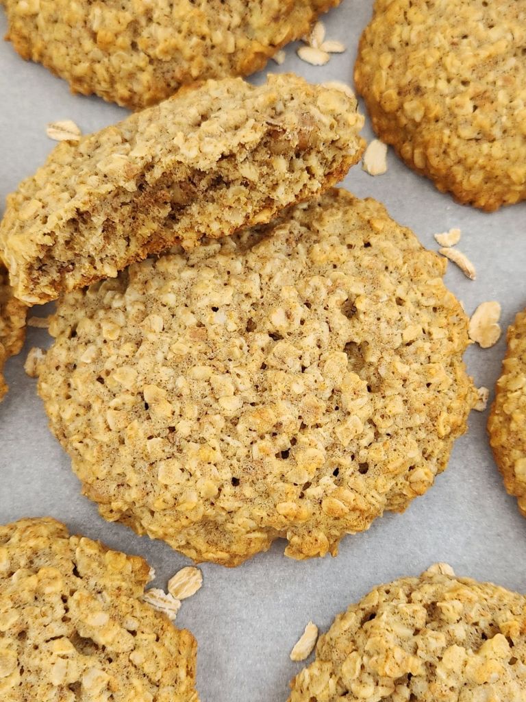 Healthy oatmeal cookie broken in half on white parchment paper, showing a soft, chewy center and golden crisp edges.