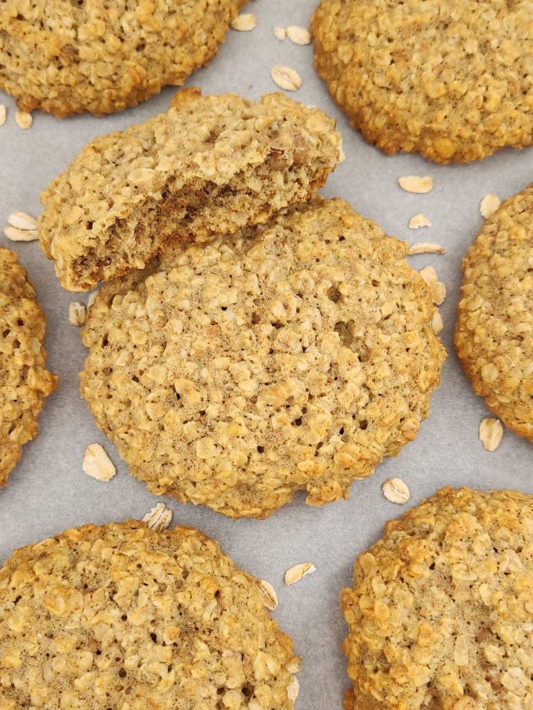 Healthy oatmeal cookie broken in half on white parchment paper, showing a soft, chewy center and golden crisp edges.