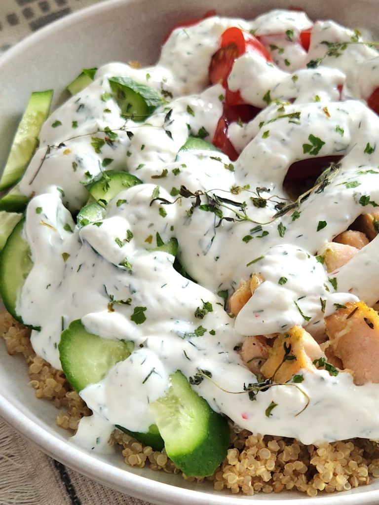 Salmon bowl with quinoa, cucumbers and tomatoes with creamy yogurt sauce with dill in a beige bowl