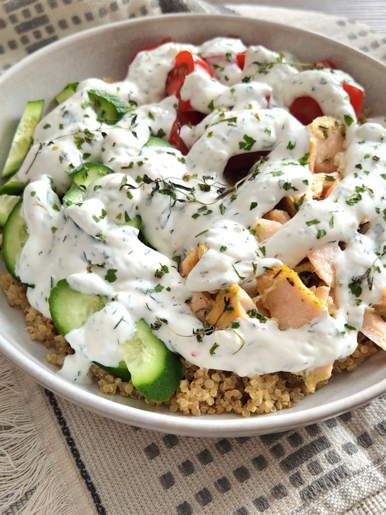 Salmon bowl with quinoa, cucumbers and tomatoes with creamy yogurt sauce with dill in a beige bowl