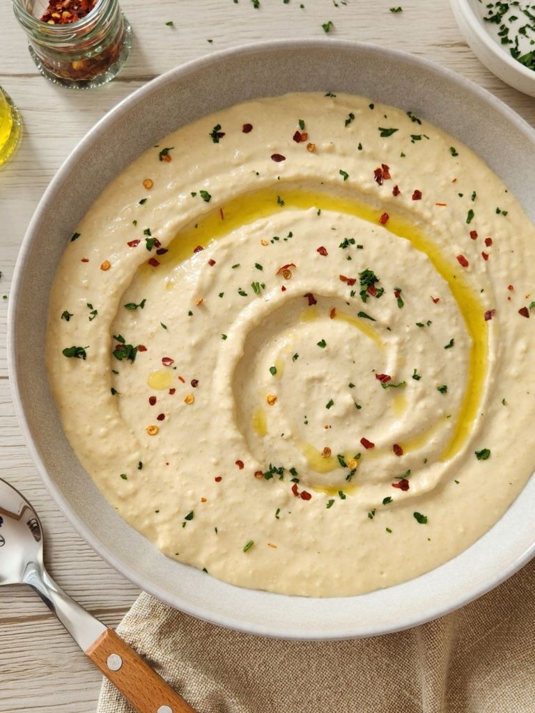 Smooth and Creamy Hummus in a beige bowl topped with olive oil, paprika and parsley 