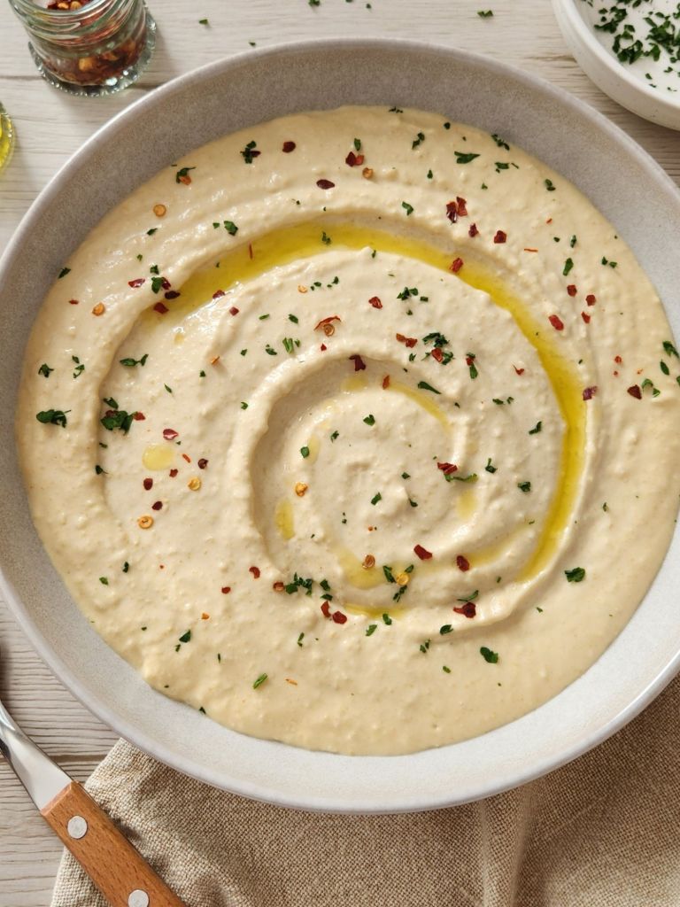Smooth and Creamy Hummus in a beige bowl topped with olive oil, paprika and parsley 