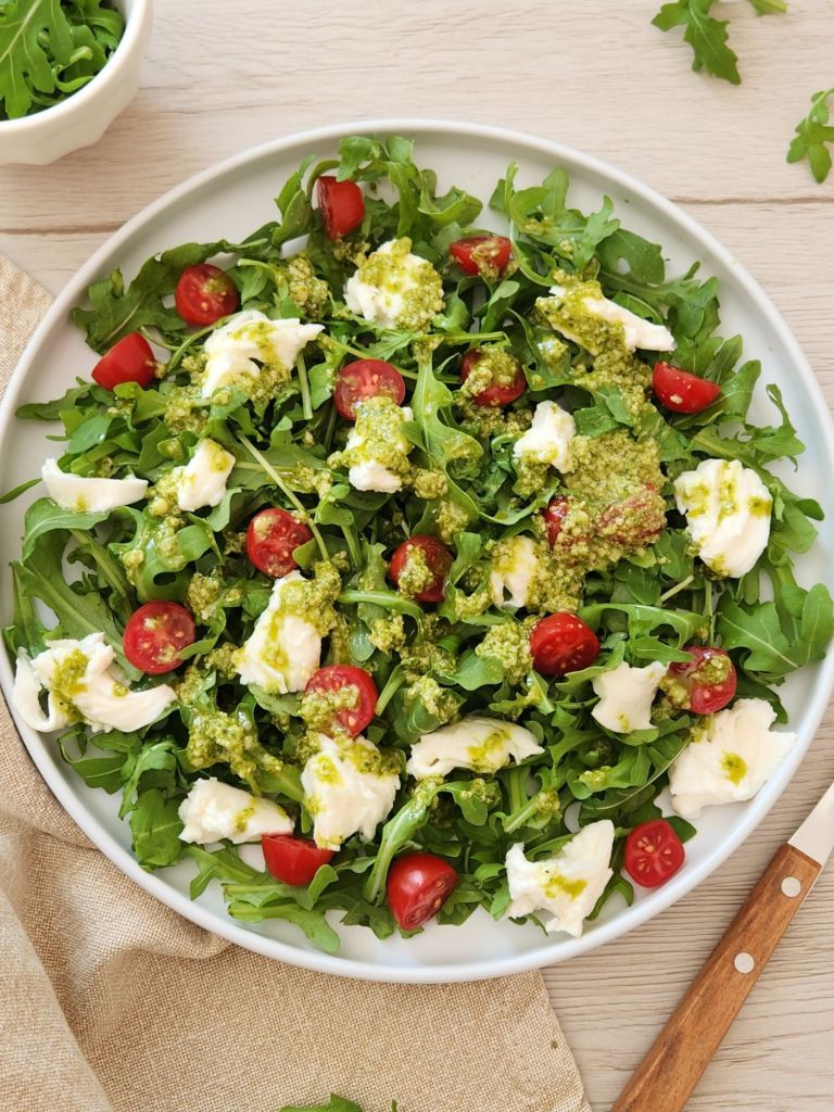 Fresh arugula mozzarella salad with pesto dressing served on a white plate