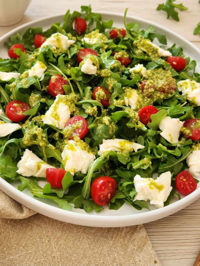 Fresh arugula mozzarella salad with pesto dressing served on a white plate