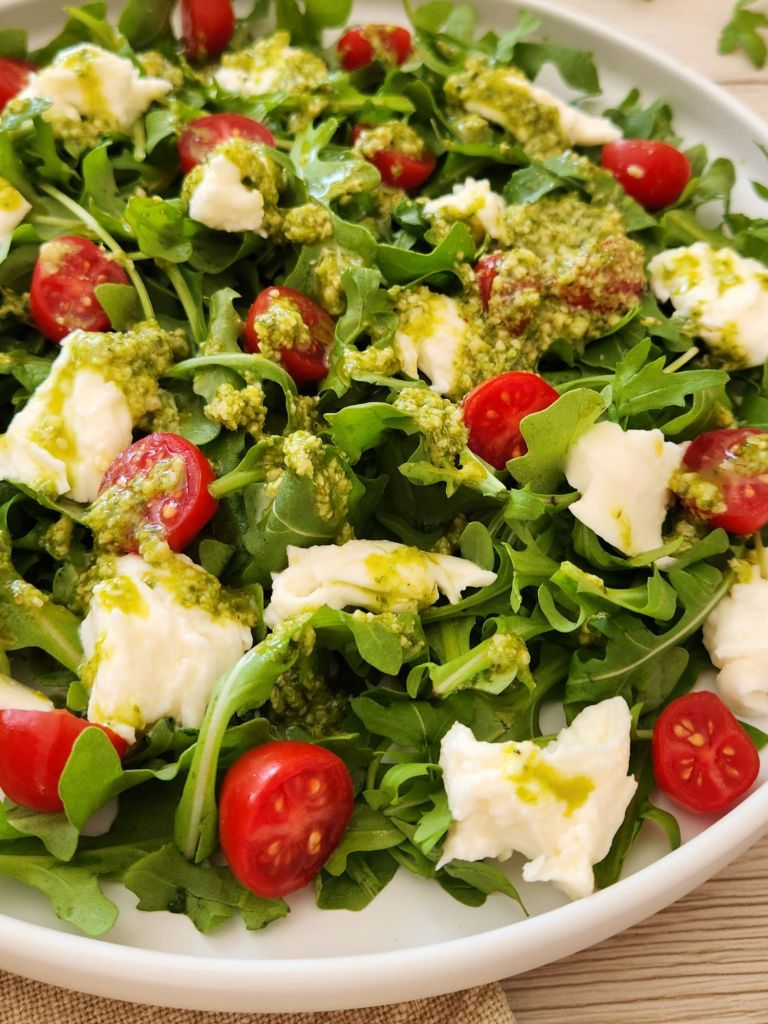 Close up of a Fresh arugula mozzarella salad with pesto dressing served on a white plate