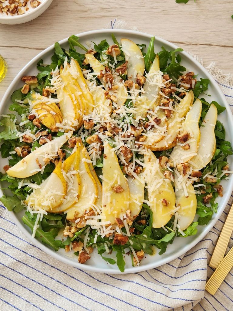 Arugula pear salad with walnuts and shaved parmesan on white plate