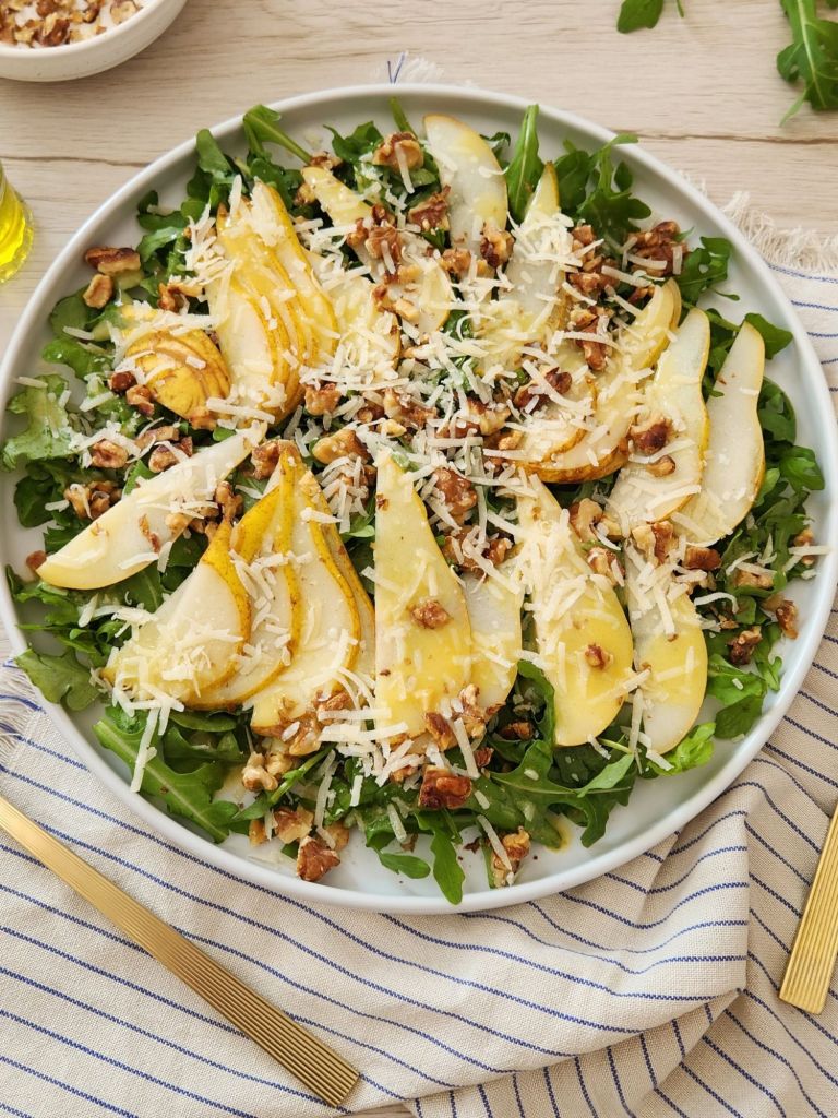 Arugula pear salad with walnuts and shaved Parmesan on white plate