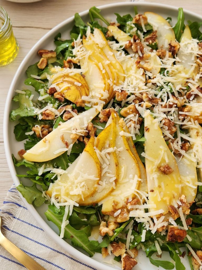 Close-up of arugula pear salad with walnuts and shaved Parmesan on white plate