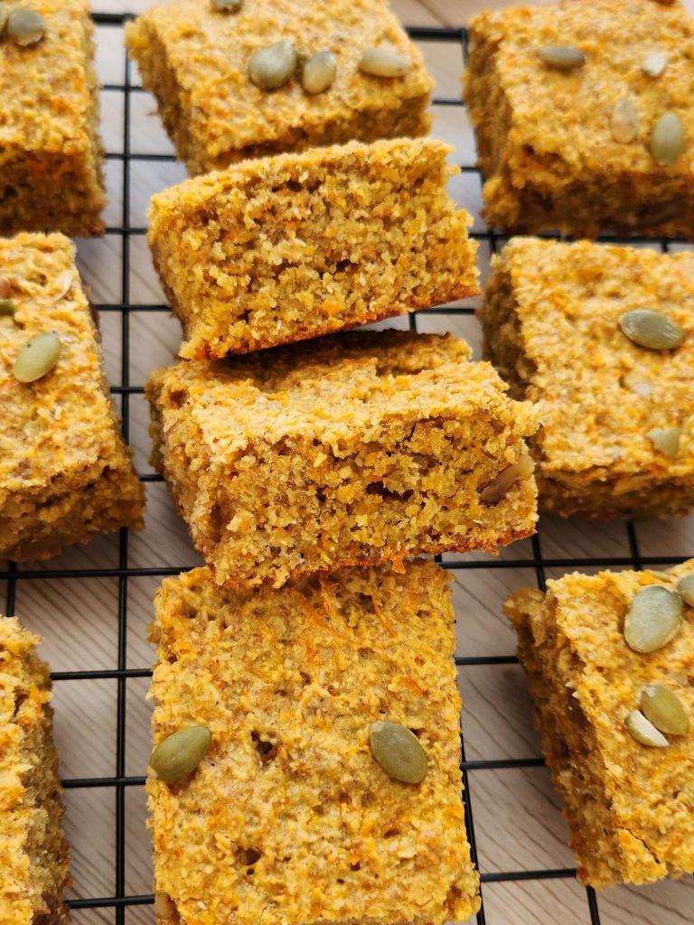 Close up of healthy carrot cake banana oat bars topped with pumpkin seeds on a cooling rack