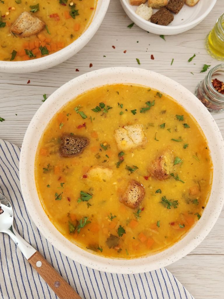 Yellow Split Pea Soup served with croutons, parsley and crushed red pepper in a beige bowl