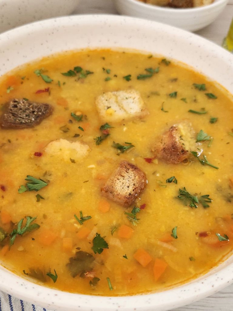 Close up of Yellow Split Pea Soup served with croutons, parsley and crushed red pepper in a beige bowl