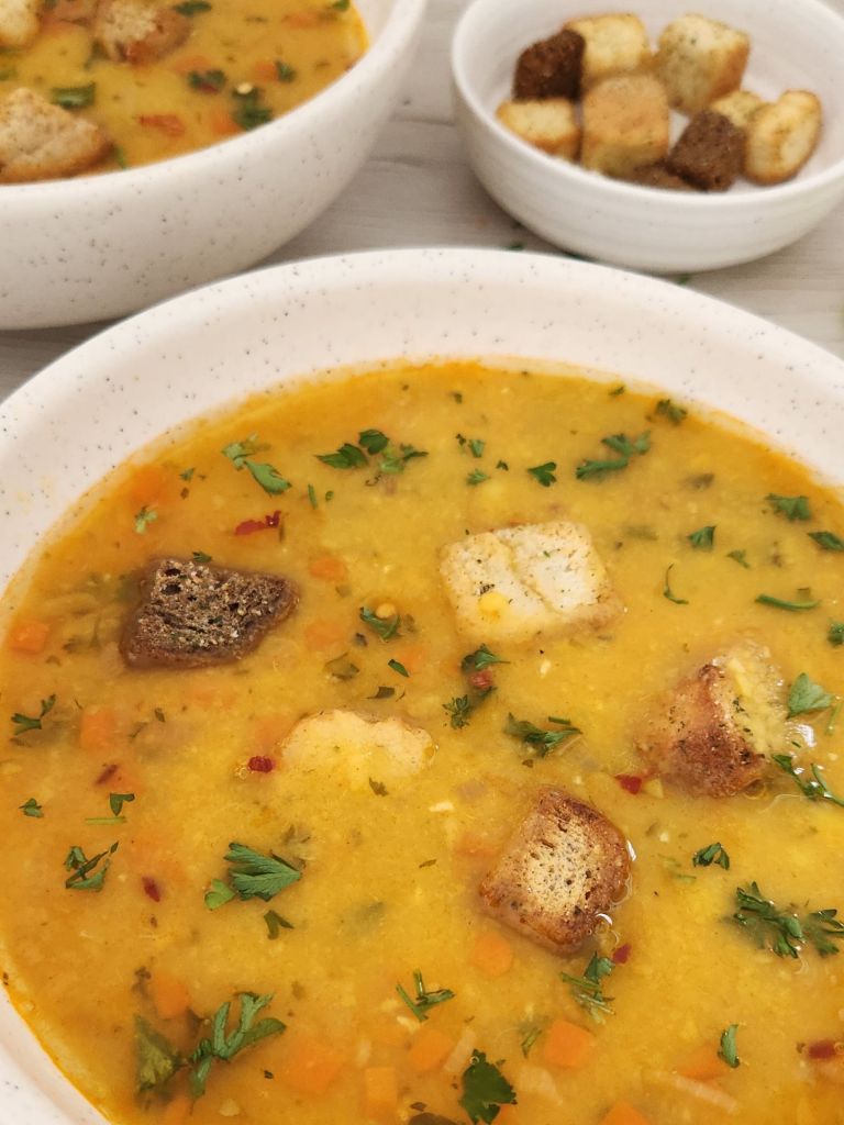 Close-up of Yellow Split Pea Soup served with croutons, parsley and crushed red pepper in a beige bowl
