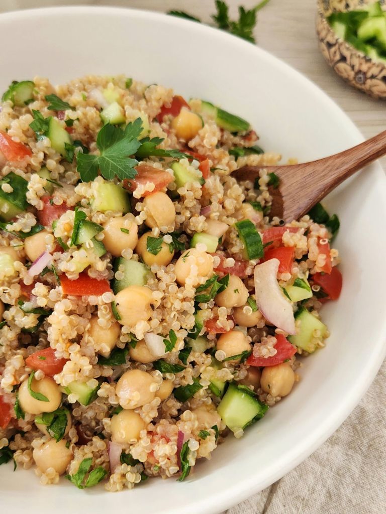Quinoa chickpea salad with cucumber, tomatoes, red onion, and parsley, served in a white bowl with lemon dressing