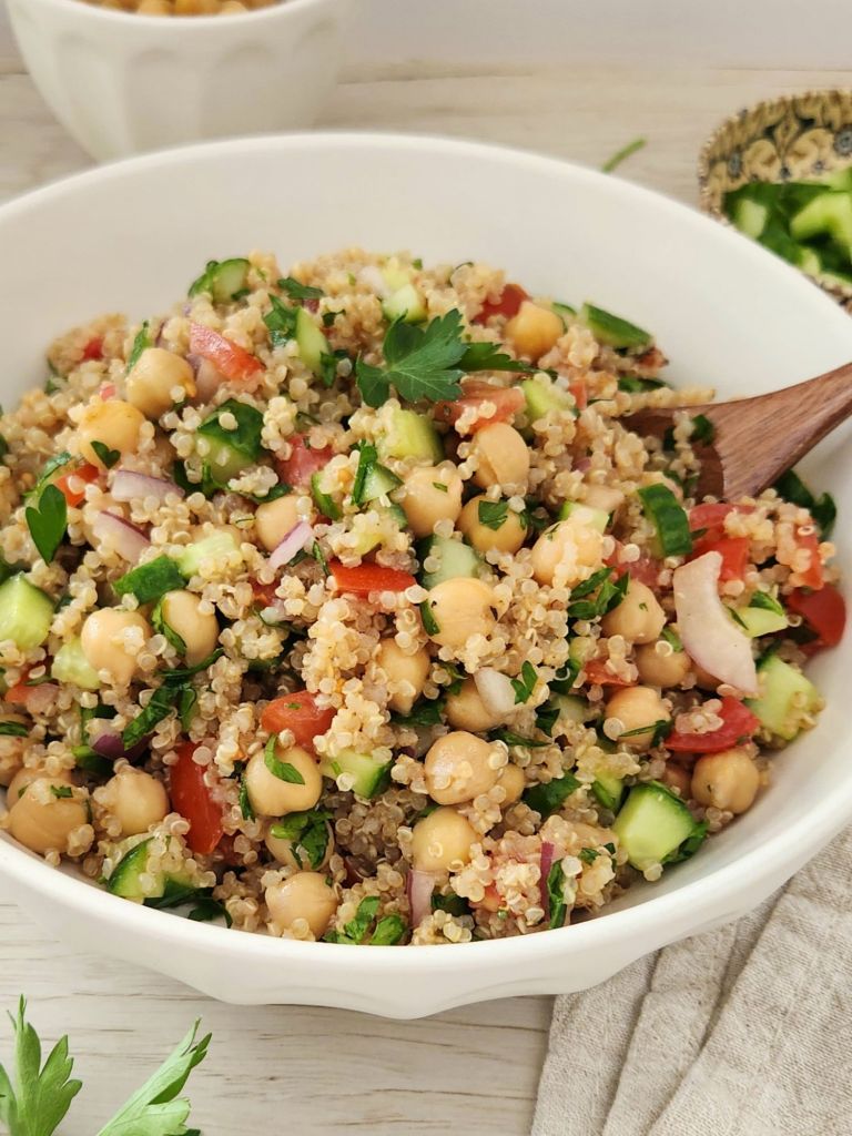 Quinoa chickpea salad with cucumber, tomatoes, red onion, and parsley, served in a white bowl with lemon dressing
