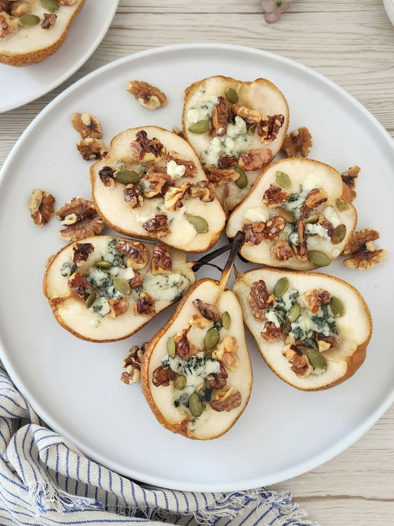 Baked pear halves with walnuts, honey, and melted blue cheese on a white plate