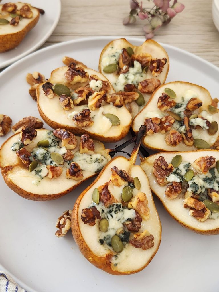 Baked pear halves with walnuts, honey, and melted blue cheese on a white plate