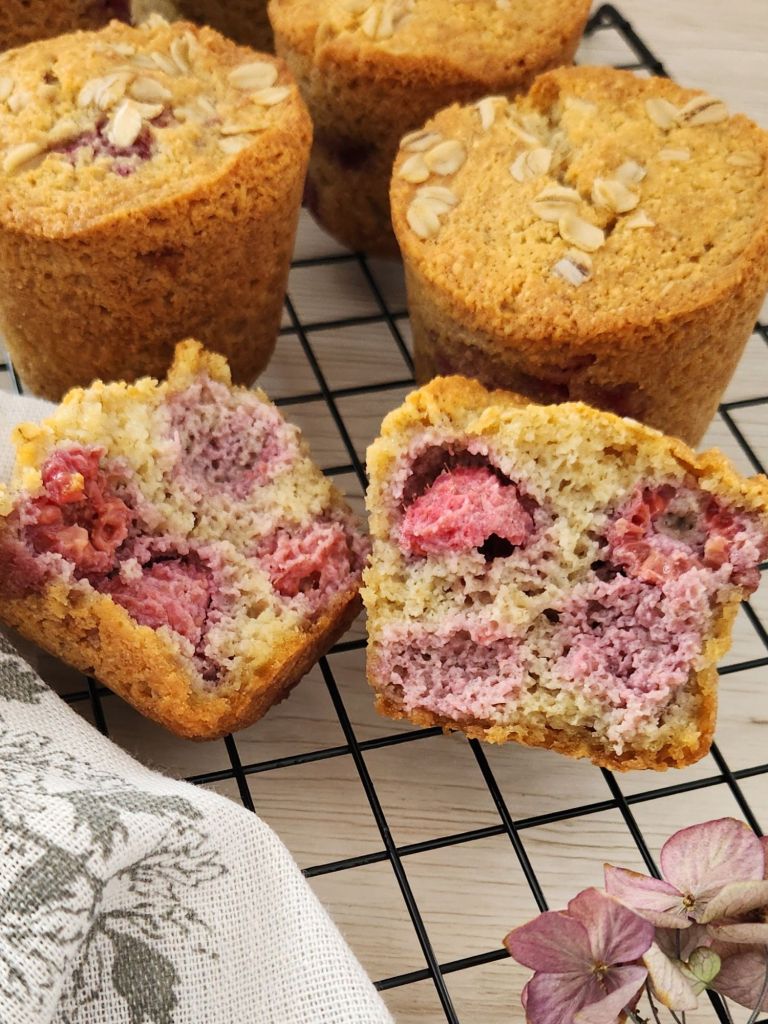 Gluten-free raspberry almond muffins on a cooling rack, with two muffins cut open to show the soft crumb and juicy raspberries inside.