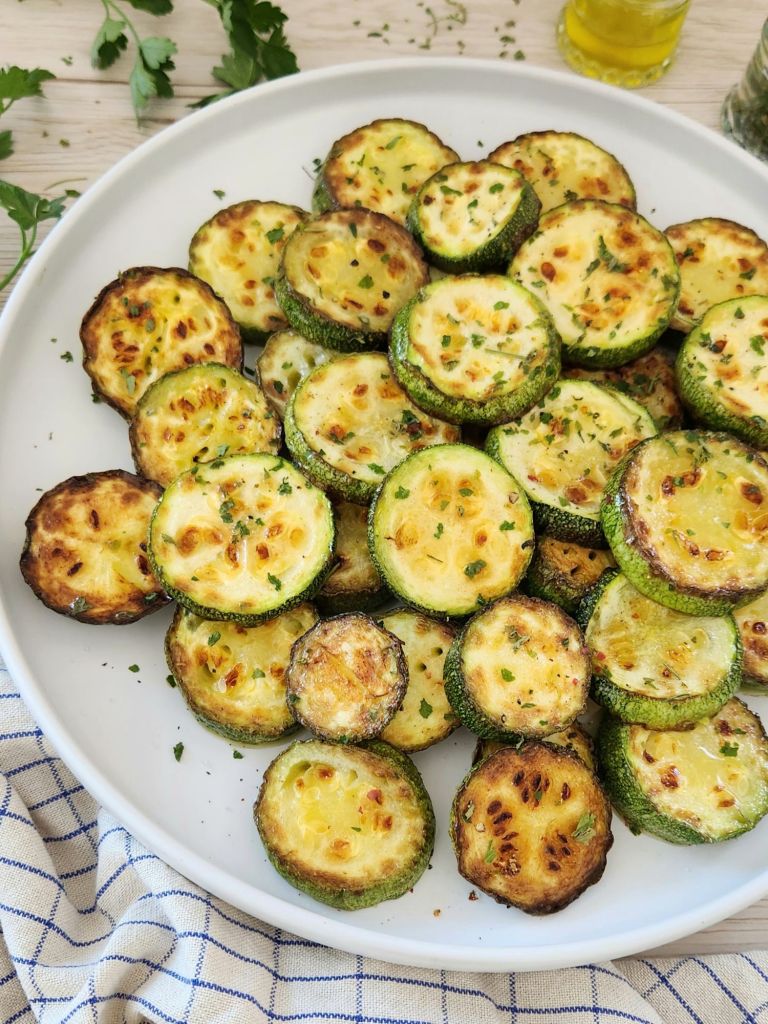 Healthy pan fried zucchini without breading, topped with parsley on a white plate