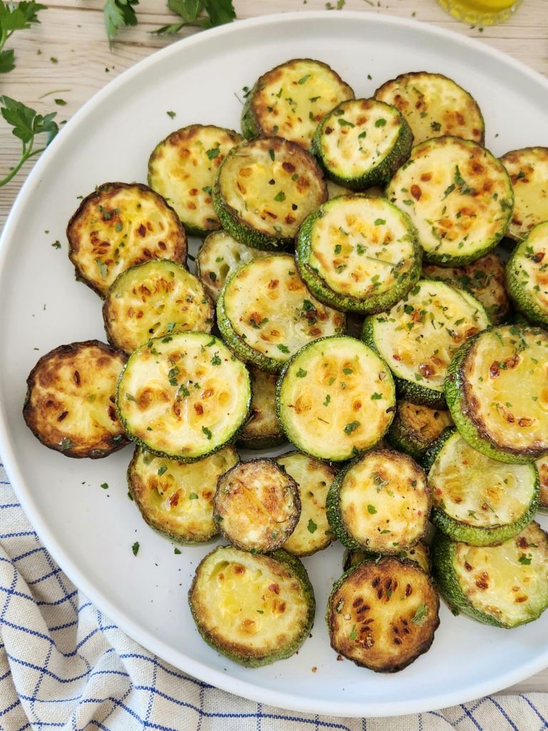 Healthy pan fried zucchini without breading, topped with parsley on a white plate