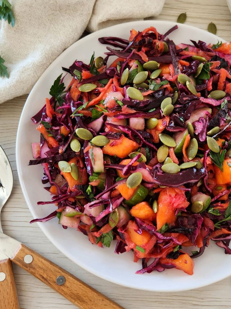 Crunchy red cabbage detox salad with carrot, mango, cucumber and pumpkin seeds served on a white plate