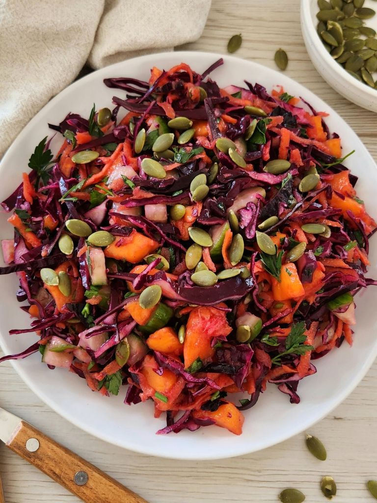 Crunchy red cabbage detox salad with carrot, mango, cucumber and pumpkin seeds served on a white plate