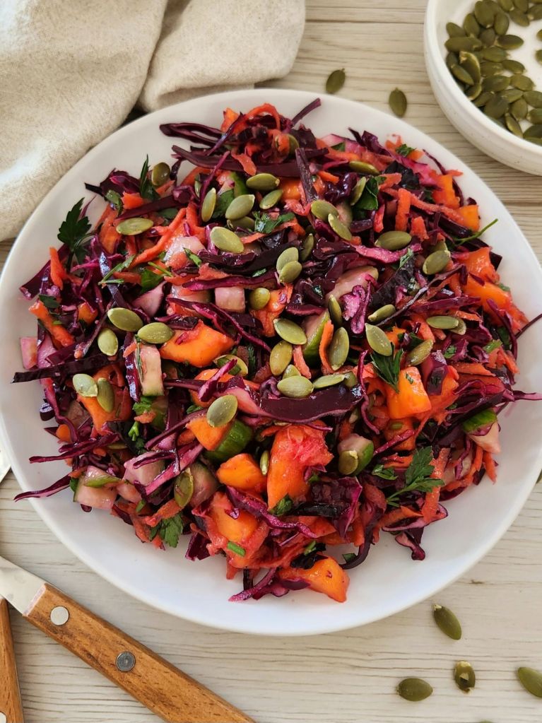 Crunchy red cabbage detox salad with carrot, mango, cucumber and pumpkin seeds served on a white plate