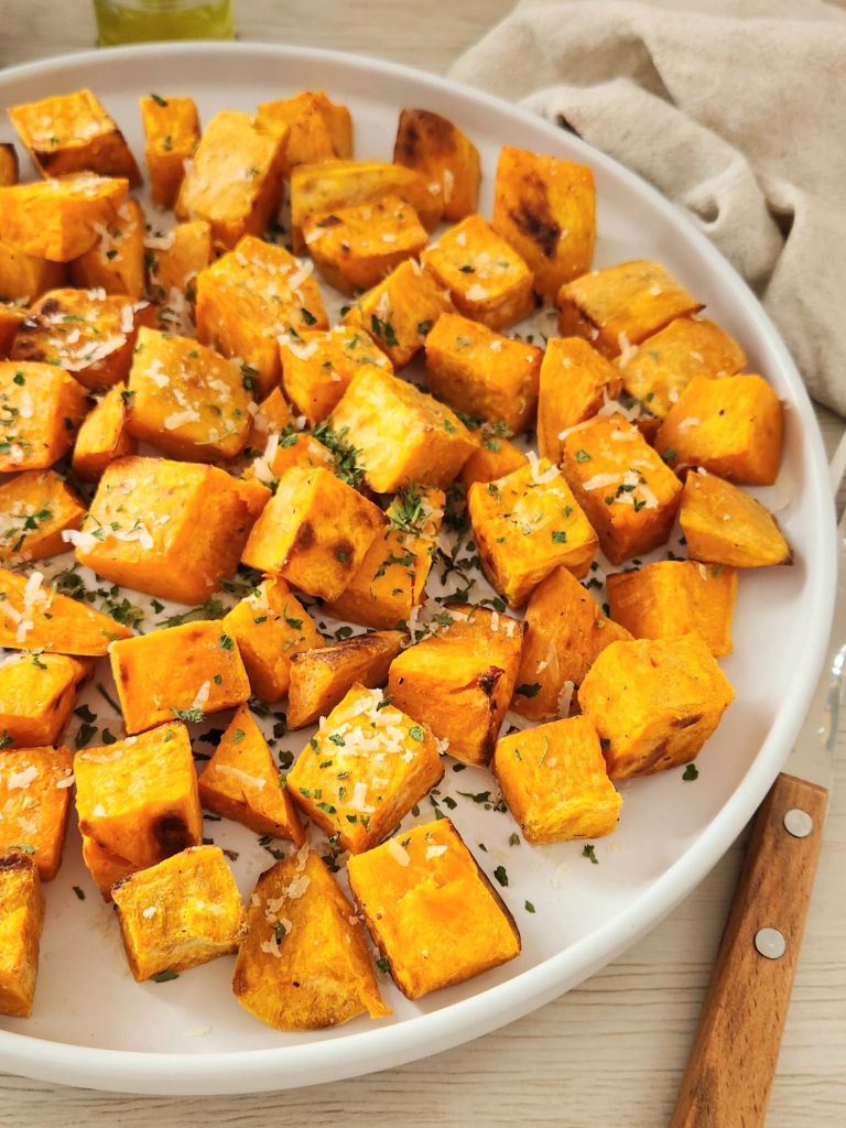 Oven baked sweet potato cubes with olive oil, parmesan and dried parsley on a white plate