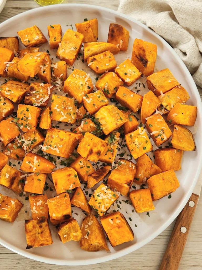 Oven baked sweet potato cubes with olive oil, parmesan and dried parsley on a white plate