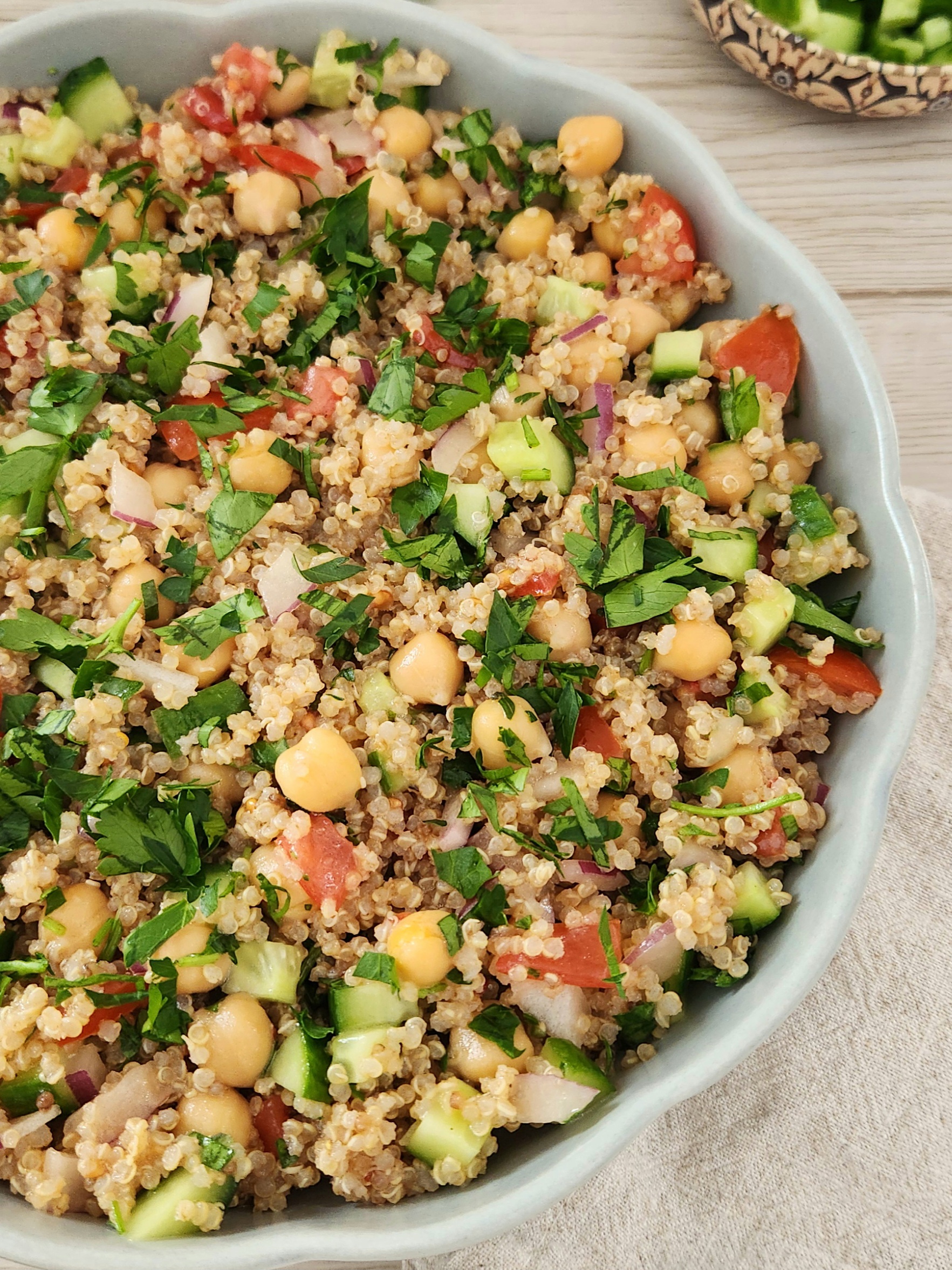 Quinoa chickpea salad with cucumber, tomatoes, red onion, parsley, and lemon dressing in a sage green bowl