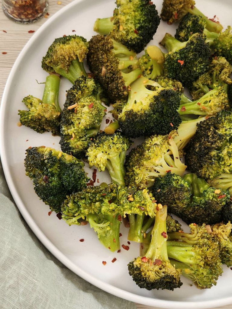 Chopped green broccoli sautéed with fresh garlic and soy sauce, served on a white plate