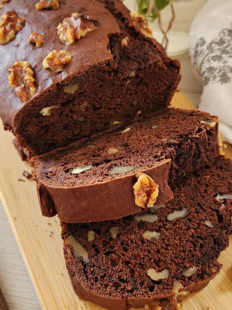 Chocolate banana bread loaf with walnuts, sliced on a wooden board, showing moist chocolate crumb and made with reduced sugar