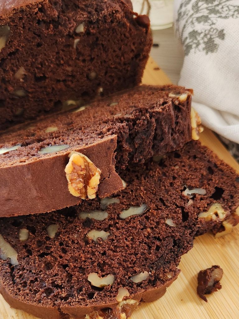 Chocolate banana bread loaf with walnuts, sliced on a wooden board, showing moist chocolate crumb and made with reduced sugar