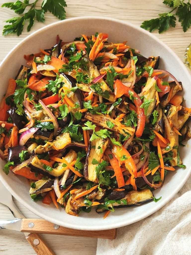 Roasted eggplant salad with fresh vegetables and honey vinegar dressing in a beige bowl