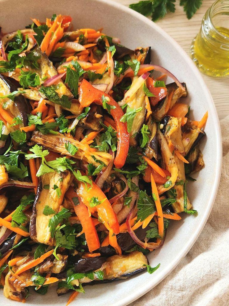 Roasted eggplant salad with fresh vegetables and honey vinegar dressing in a beige bowl