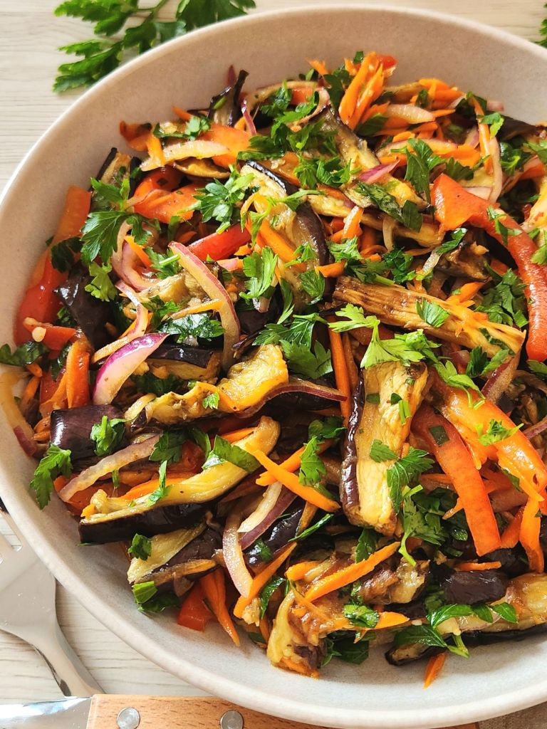 Roasted eggplant salad with fresh vegetables and honey vinegar dressing in a beige bowl