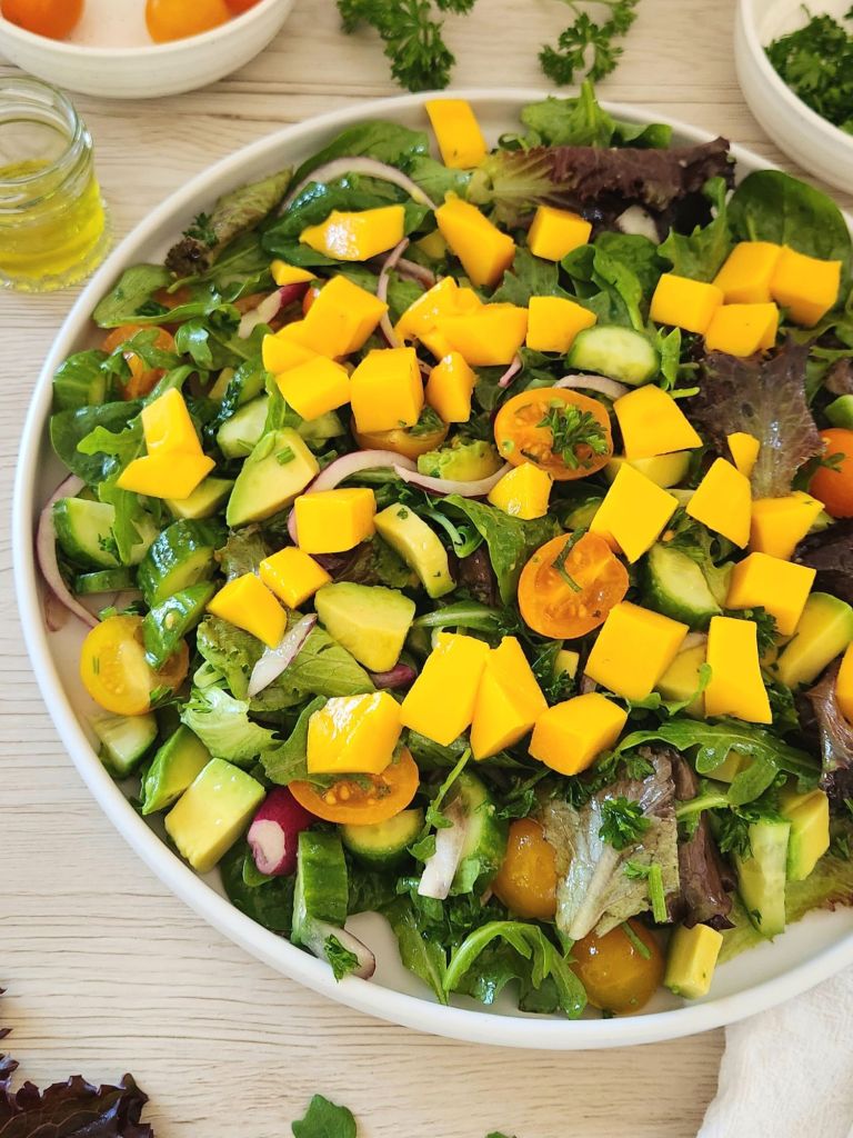 Mango avocado salad with spring mix, cherry tomatoes, cucumber, and lime dressing on a white plate