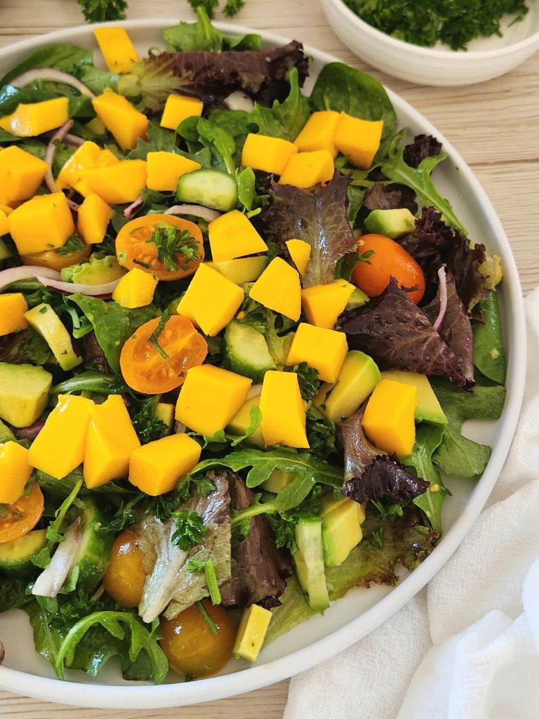 Mango avocado salad with spring mix, cherry tomatoes, cucumber, and lime dressing on a white plate