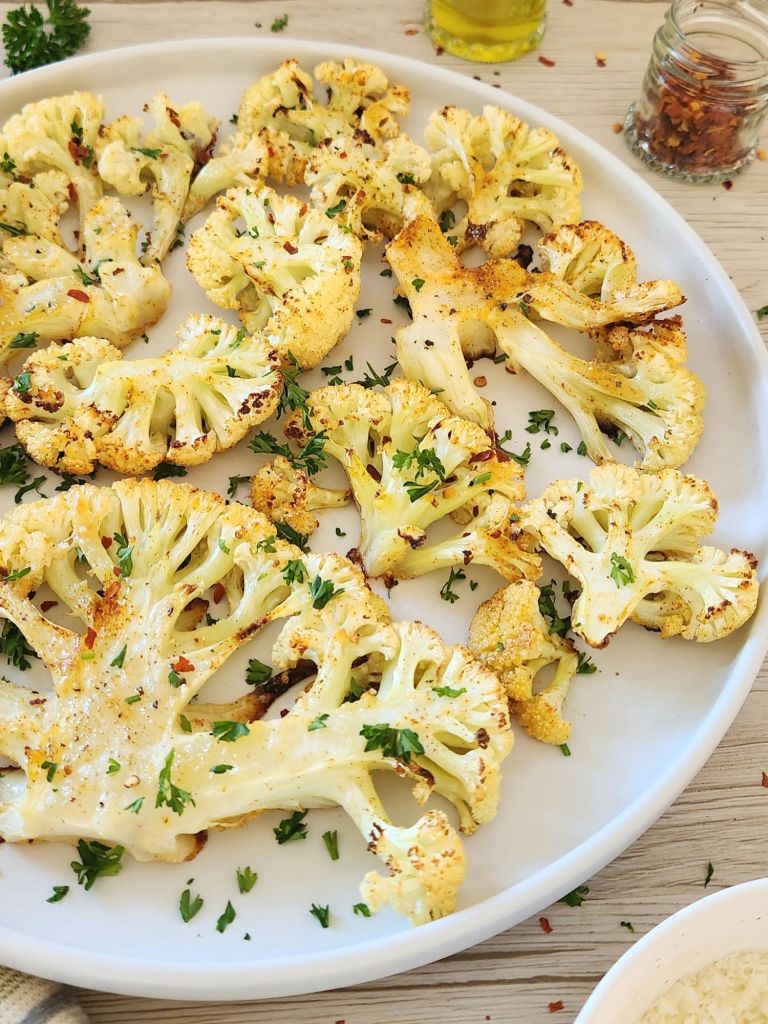 Golden roasted cauliflower with parmesan topped with fresh parsley on a white plate